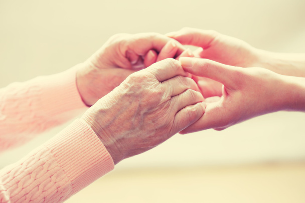 Old and young holding hands on light background, closeup - Foto, afbeelding