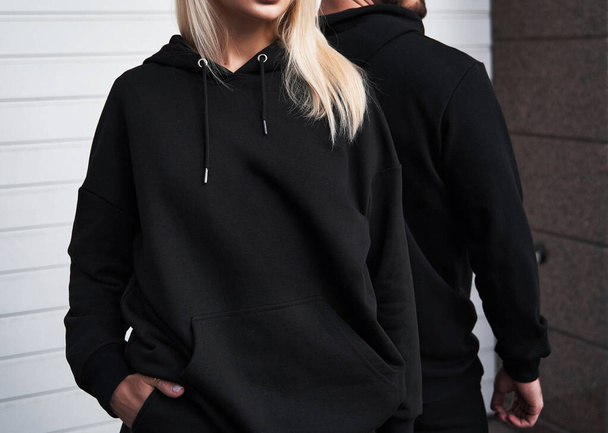 Βασική μάρκα ρούχων mockup. Πρότυπο σχεδιασμού για hoodie και casual αθλητικά ενδύματα. Μια γυναίκα και ένας άντρας που φοράνε κουκούλες χωρίς λογότυπο. Οριζόντια μακέτα φούτερ - Φωτογραφία, εικόνα
