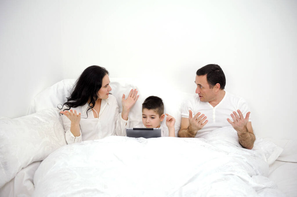 home disagreements parents quarrel in bed under covers son boy with tablet in hands family violence inattention to children a lonely child not pedagogical education psychological problems conflicts - Фото, изображение