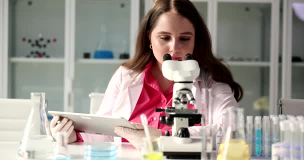 Young female scientist using microscope touchpad in laboratory. Microscope and microscopic research methods - Footage, Video
