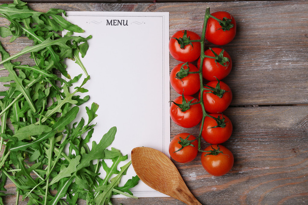 Menu sheet of paper with cherry tomatoes and arugula on rustic wooden surface background - Фото, изображение