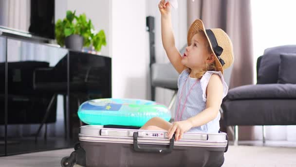 Little girl in suitcase baggage luggage and inflatable life buoy playing with toy plane and ready to go for traveling on vacation. High quality 4k footage - Filmati, video