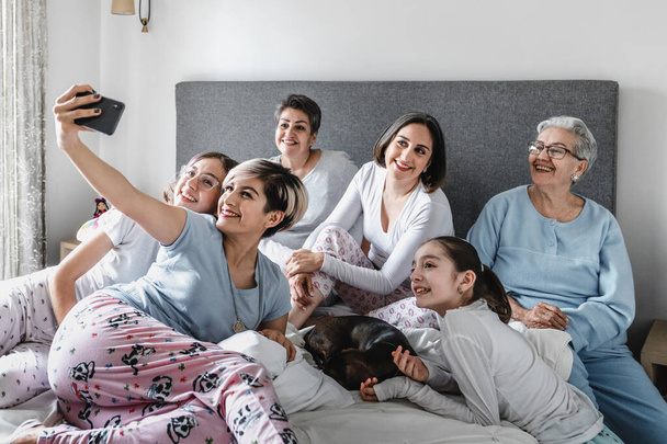 Hispanic happy family of women, grandmother, daughter and children laughing taking a photo selfie on bed at home in Latin America - Photo, image