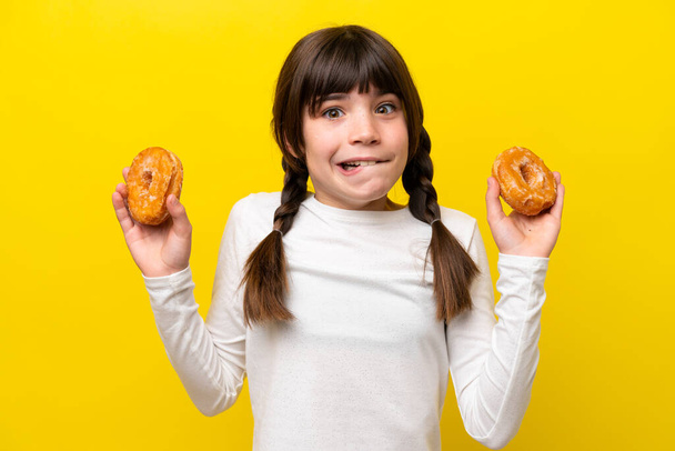 Kleine kaukasische Mädchen isoliert auf gelbem Hintergrund halten Donuts - Foto, Bild