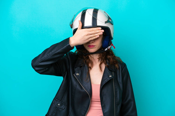 Junge kaukasische Frau mit Motorradhelm auf blauem Hintergrund, die die Augen mit den Händen verdeckt. Wollen nichts sehen - Foto, Bild