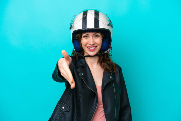 Молода біла жінка з мотоциклетним шоломом ізольована на синьому фоні, трясучи руки для закриття багато угоди
 - Фото, зображення