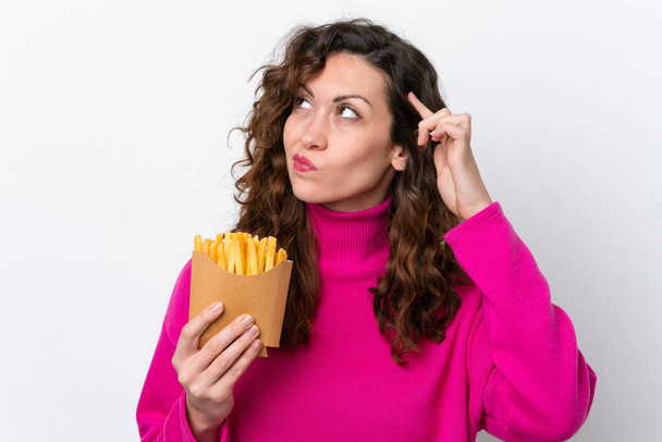 Giovane donna caucasica cattura patatine fritte isolate su sfondo bianco avendo dubbi e con espressione faccia confusa - Foto, immagini