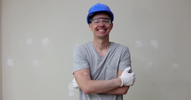 Young smiling repairman in a helmet and rendering repair finishing work indoors. Professional repairman during work - Filmati, video