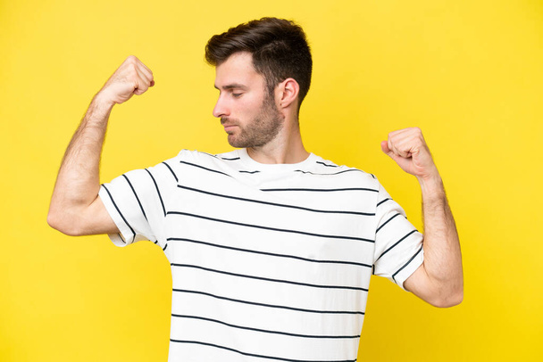 Young caucasian man isolated on yellow background doing strong gesture - Φωτογραφία, εικόνα