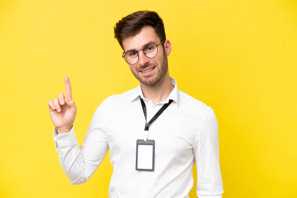 Young caucasian with ID card isolated on yellow background showing and lifting a finger in sign of the best - Fotografie, Obrázek