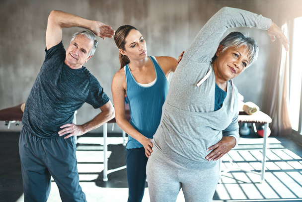 Stay physical, stay flexible. a senior man and woman working out with the help of an instructor - Foto, Imagem