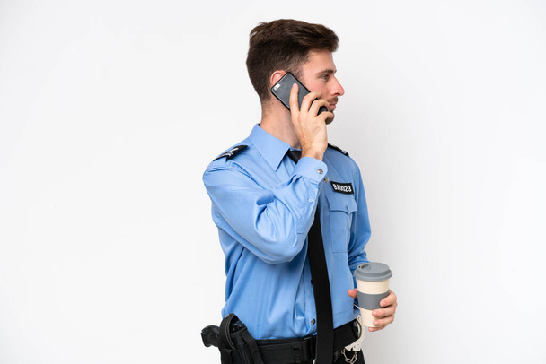 Young police caucasian man isolated on white background holding coffee to take away and a mobile - Fotó, kép