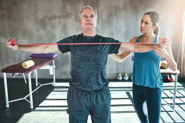 Muskelschwäche muss kein Ding der Unmöglichkeit sein. ein älterer Mann, der mit Hilfe eines Physiotherapeuten Widerstandsbänder benutzt - Foto, Bild