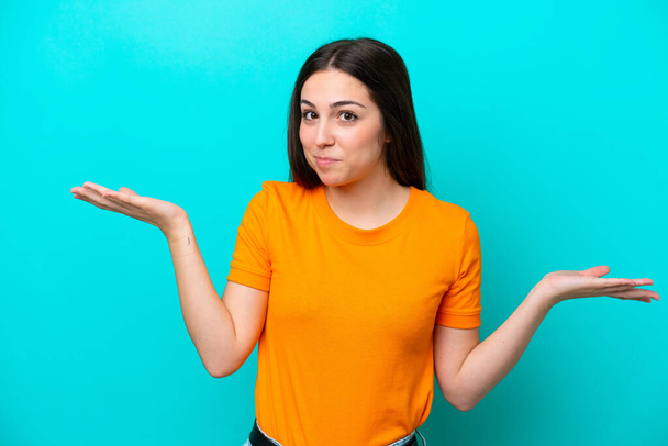 Young caucasian woman isolated on blue background having doubts while raising hands - Foto, afbeelding