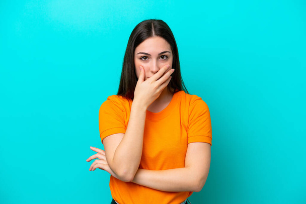 Junge kaukasische Frau isoliert auf blauem Hintergrund, der Mund mit der Hand bedeckt - Foto, Bild