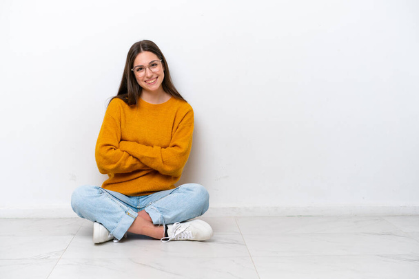 Young girl sitting on the floor isolated on white background with arms crossed and looking forward - Zdjęcie, obraz