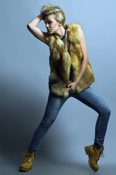 Emocionální portrét nádherná blonďatá modelka v džínách a příležitostné vesta vystupují nad modrým pozadím. Studio záběr. Hipster styl. Kopírovat prostor - Fotografie, Obrázek