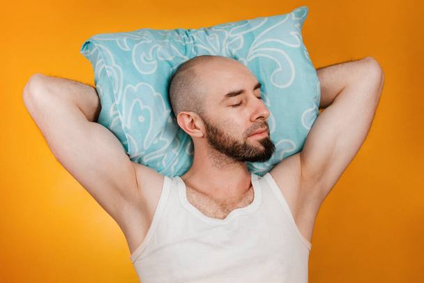 The concept of rest. Man, folding his hands under his pillow, sleeps overuses to the side. Orange background. - Photo, image