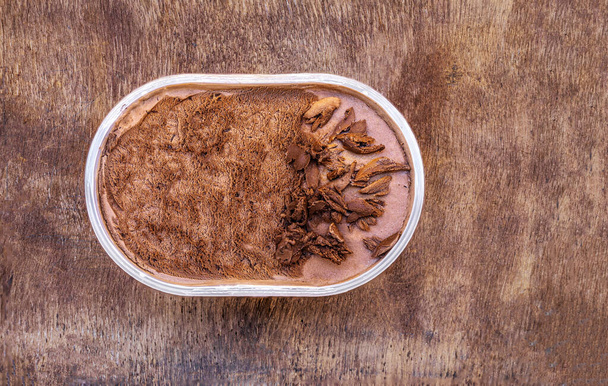 Chocolate icecream on a wooden rustic background. Dark chocolate  ice cream in a conteine - Photo, Image