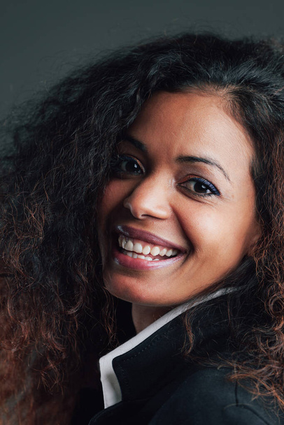 Portrait of Black-skinned Woman with long wavy hair, in elegant white shirt and black jacket. Smiling, happy expression with perfect teeth - Zdjęcie, obraz