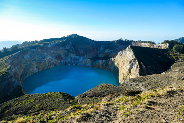 View on the Kelimutu volcanic crater lakes in Flores, Indonesia. Lakes are shining with many shades of turquoise and blue. Sun shines through clouds. Barren and sharp slopes of the volcanic crater - Foto, Imagen