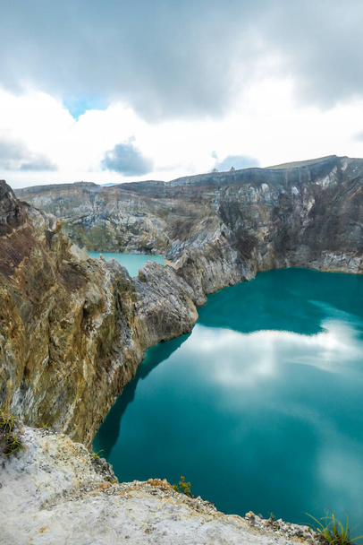 View on the Kelimutu volcanic crater lakes in Flores, Indonesia. Lakes are shining with many shades of turquoise and blue. Sun shines through clouds. Barren and sharp slopes of the volcanic crater - Foto, Imagen