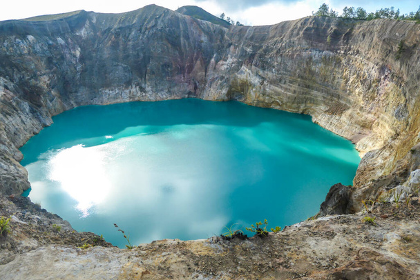 Close up view on the Kelimutu volcanic crater lakes in Flores Indonesia. Lakes are shining with many shades of turquoise and blue. Sun shines through clouds. Barren and sharp slopes of volcanic crater - Foto, Imagen