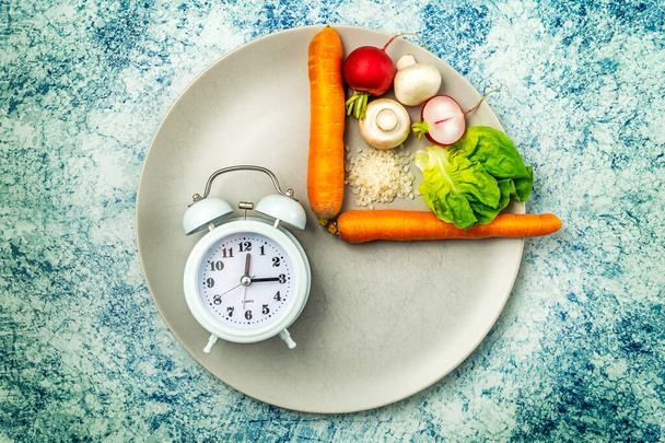 Intermittent fasting diet concept. One fourth plate with healthy food and three fourths plate is empty. Champignon mushrooms, carrots, lettuce, rice, red radish. Blue rustic background. Top view. - 写真・画像