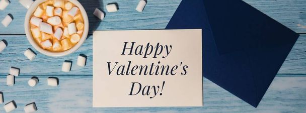 HAPPY VALENTINES DAY text Banner blue envelope with white cup of coffee and marshmallows on wooden blue background. holiday. Top view, flat lay minimalist branding concept - Photo, Image