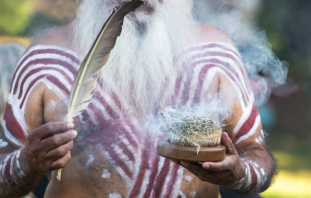 Avustralyalı Aborjin sigara içme seremonisi, erkek eli yanan bitkilerin dumanını tutuyor, toplumsal etkinlikte ayin, yerel kültürün ve geleneklerin sembolü. - Fotoğraf, Görsel