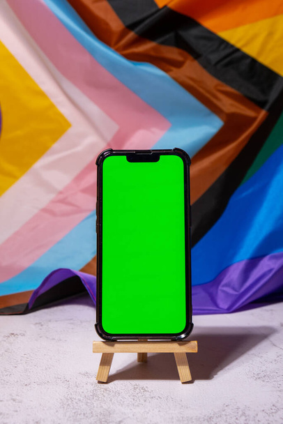 Mobile phone with chroma key on Rainbow LGBTQIA flag made from silk material background. Happy pride month. Symbol of LGBTQ pride month. Equal rights. Peace and freedom. Support LGBTQIA community - 写真・画像