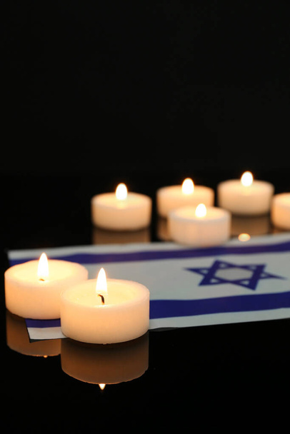Burning candles with flag of Israel on dark background, closeup. International Holocaust Remembrance Day - Photo, Image