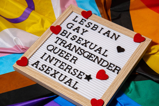 LGBTQIA description frame on Rainbow LGBTQIA flag made from silk material. LESBIAN, GAY, BISEXUAL, TRANSGENDER, QUEER, INTERSEX, ASEXUAL. Symbol of LGBTQ pride month. Equal rights. Peace and freedom - Zdjęcie, obraz
