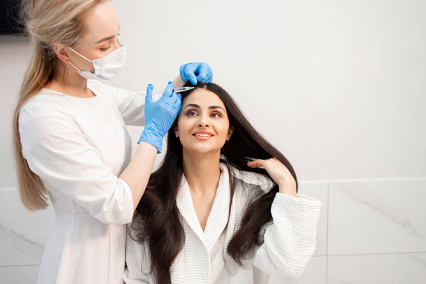 zabieg mezoterapii włosów w klinice kosmetologii, lekarz kosmetolog wykonuje wstrzyknięcie toksyny botulinowej do głowy dziewczyny - Zdjęcie, obraz