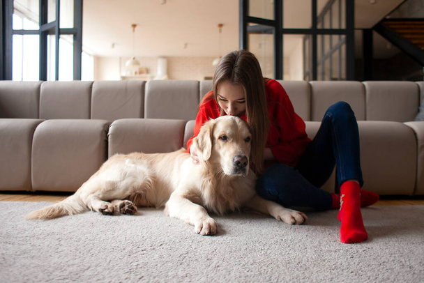young girl plays with dog breed golden retriever at home on the floor, woman with pet together lies on mat near the sofa - Fotoğraf, Görsel