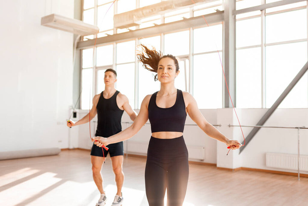 beautiful athletic couple in sportswear jumping rope in the gym in the morning, fitness girl and coach man go in for sports in training in bright room - Φωτογραφία, εικόνα