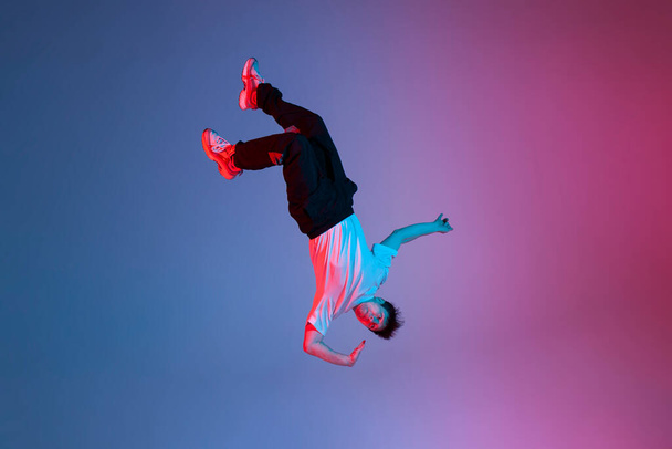 young guy falls upside down in the air, man levitates and flies down in neon lighting, acrobat dancer flies in a jump, concept of dreams and fantasies - Foto, Imagen
