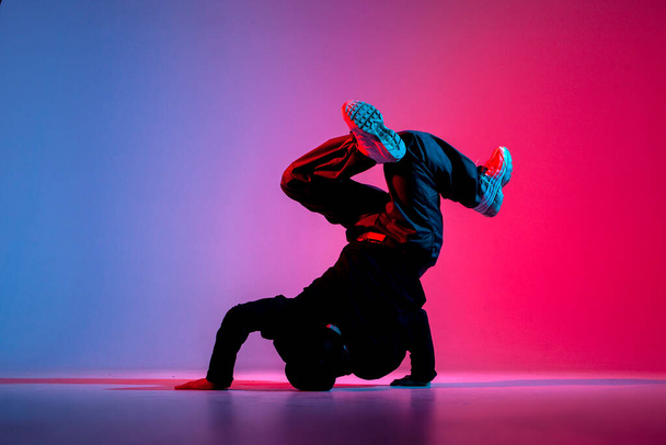 dancer doing acrobatic trick and dancing breakdance in neon red and blue lighting, young energetic guy stands on his hands in unusual pose, street style - Zdjęcie, obraz