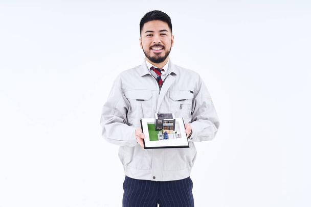 A man in work clothes with a house model and white background - Fotó, kép