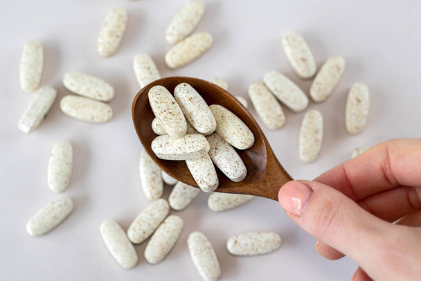 A full wooden spoon of oval beige tablets with speckles on a beige background. Supplement with a complex of vitamins. Close-up - Foto, Imagen