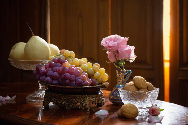 still life with plates full of fruits and flowers in vase on wooden background - Foto, afbeelding