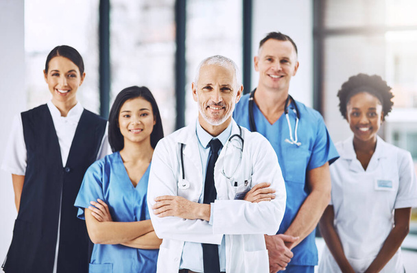 Were the only team you need. Cropped portrait of a handsome mature male doctor standing with his arms folded with his team behind him - Foto, Bild