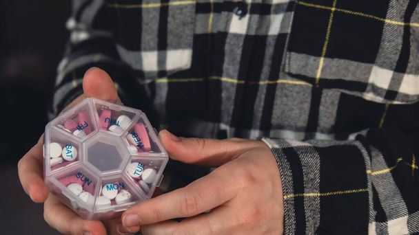 Weibliche Hände sortieren Tabletten Organizer wöchentliche Aufnahmen Nahaufnahme der medizinischen Tablettenbox mit Tabletten für die tägliche Einnahme von Medikamenten mit weiß-rosa Medikamenten und Kapseln. Junge Frau bekommt ihre täglichen Vitamine - Foto, Bild