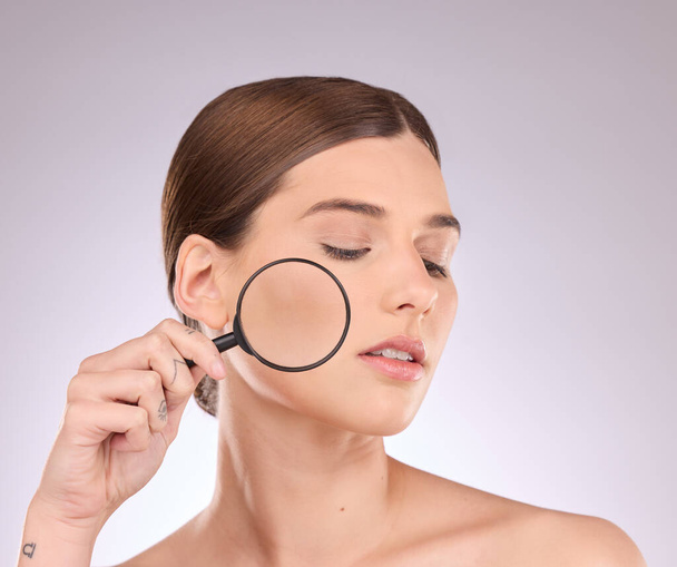 Woman, magnifying glass and face in studio for beauty, cosmetics and dermatology. Facial magnifier, female model and check skincare, aesthetic wellness and inspection for acne, laser and search pores. - Photo, Image