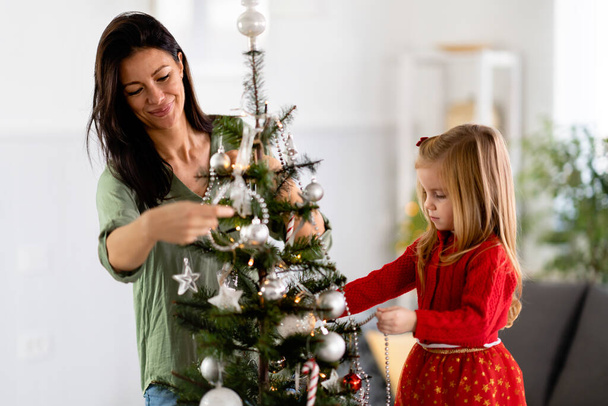 mooie moeder en dochter versieren kerstboom - Foto, afbeelding
