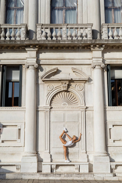 Fit αθλητικογράφος σε λευκό bodysuit και sneakers που εκτείνεται σε παγκάκι κοντά στο αρχαίο κτίριο στη Βενετία  - Φωτογραφία, εικόνα