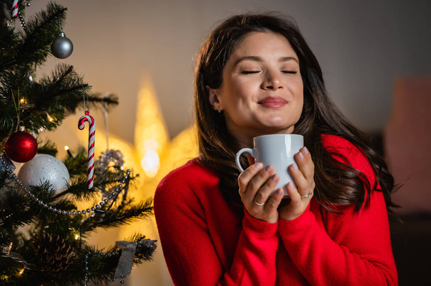beautiful young pregnant woman with cup of coffee near christmas tree - Foto, afbeelding
