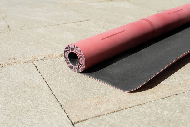 pink fitness mat with shadow on asphalt sidewalk on urban street in sunny day, summertime  - Photo, Image