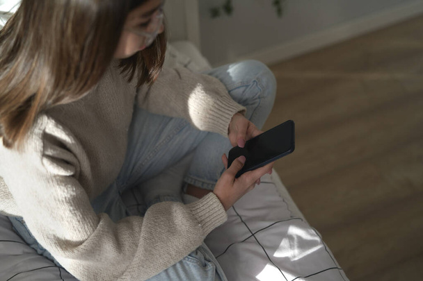 High angle view of caucasian teenage girl browsing phone while sitting on bed - Foto, Imagen