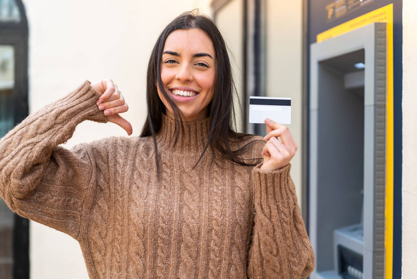 Young woman holding a credit card at outdoors proud and self-satisfied - Photo, Image